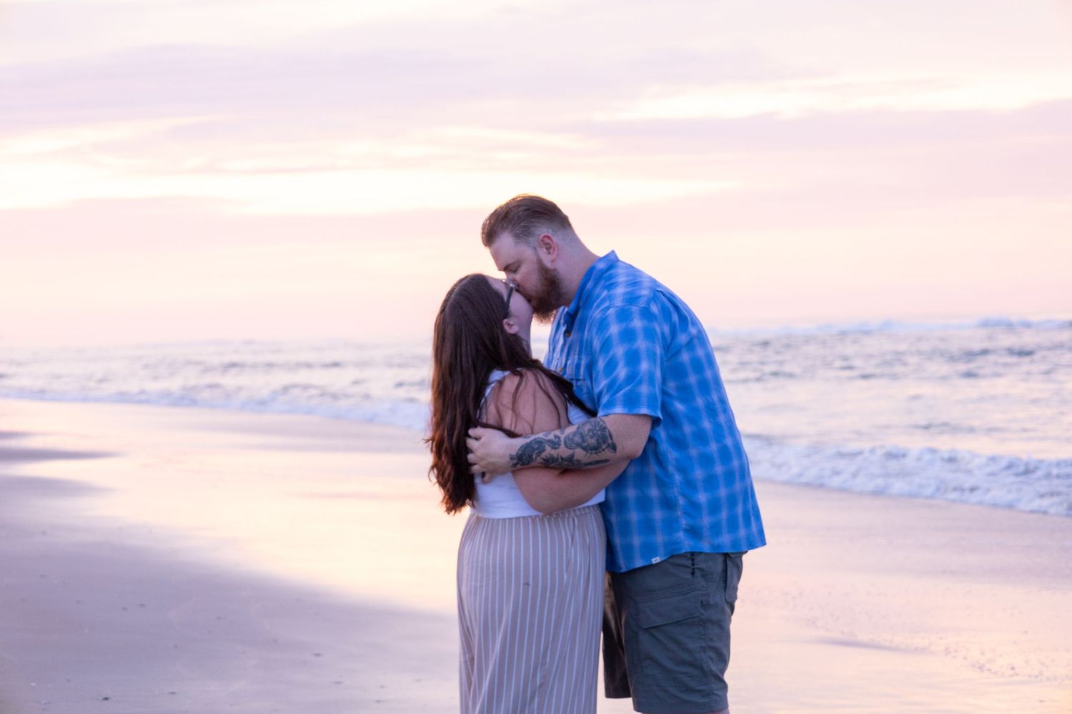 Romantic couple embracing on beach at sunset with ocean waves in background.
