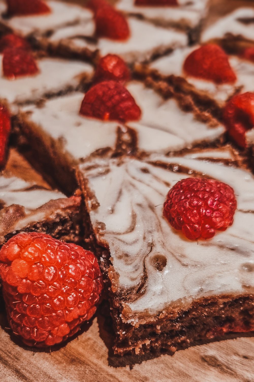 Close-up of chocolate brownies decorated with fresh red raspberries and swirled frosting.