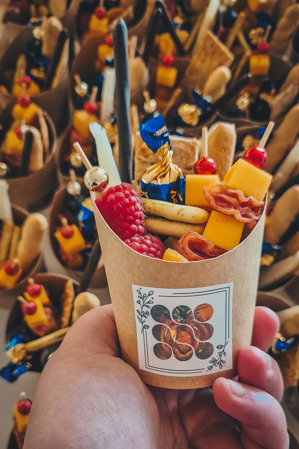Paper cup filled with colorful candy, chocolates, and berries arranged for party favors.