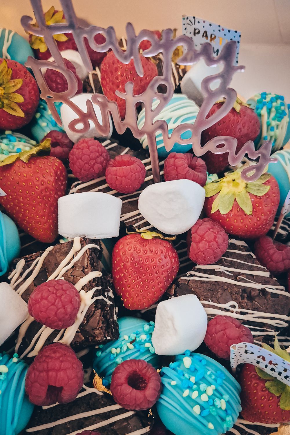 Colorful dessert platter with chocolate covered strawberries, raspberries, and decorated cookies drizzled in blue icing.