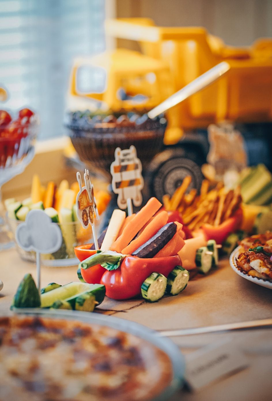 Colorful party spread with fresh vegetables, sushi rolls and snacks beside a yellow toy truck.