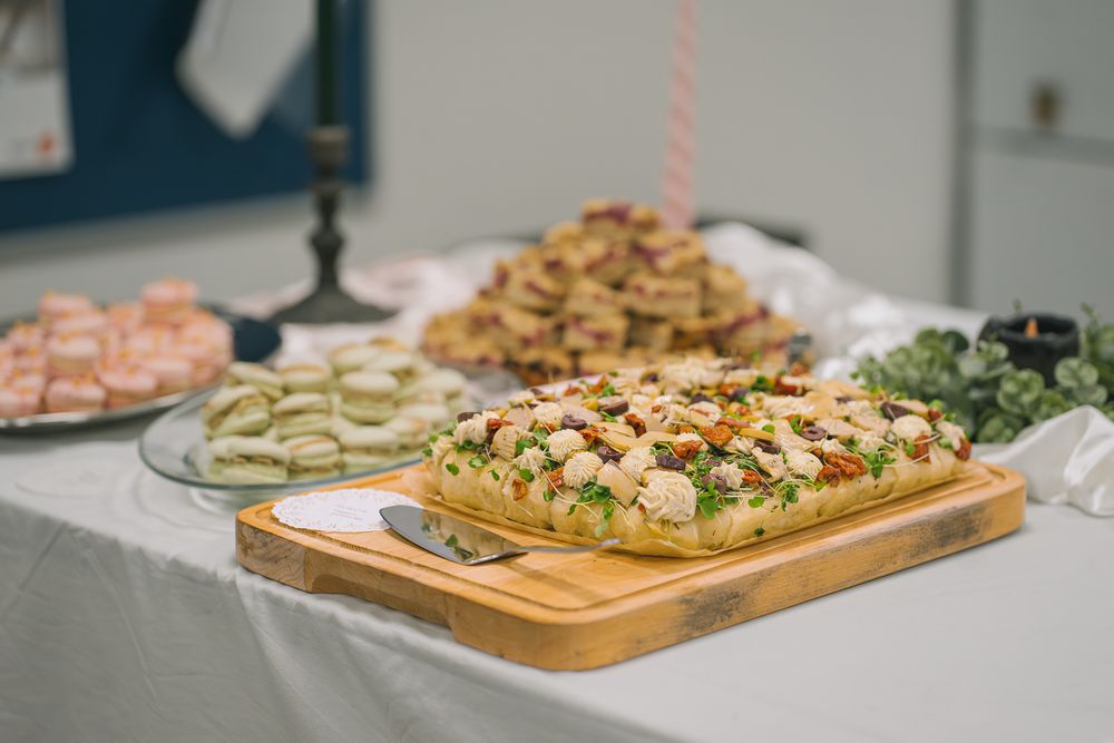 A wooden serving board displays cucumber sandwiches alongside other party platters of appetizers at a catered event.