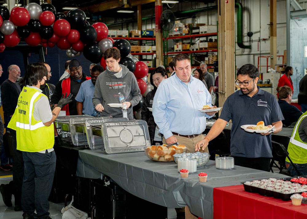 People serving food at buffet table with red balloon decorations.