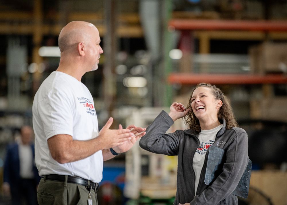 Colleagues interacting and laughing together in an industrial workplace setting.