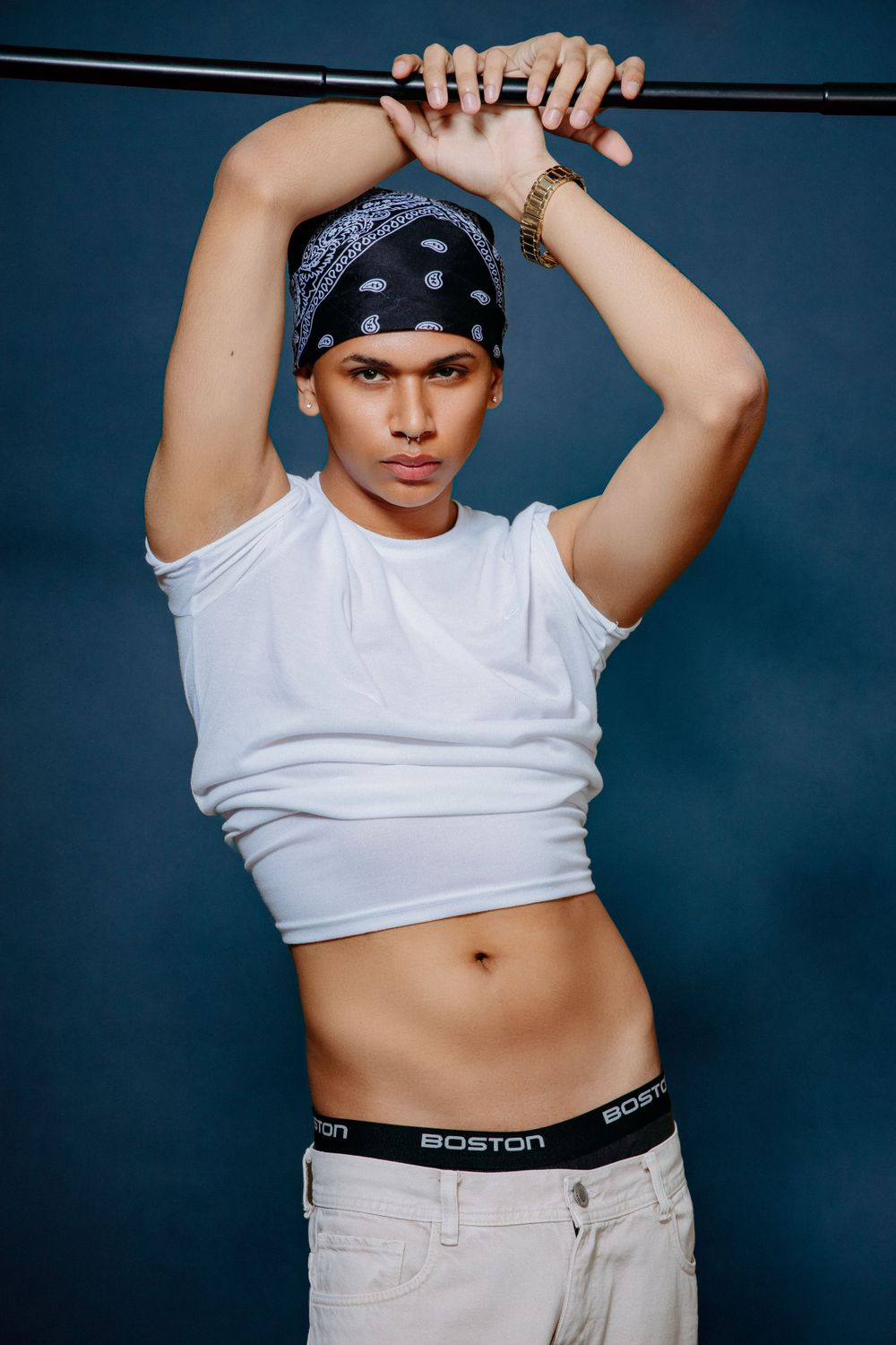 Fashion portrait of a model in white tank top and bandana against blue backdrop.