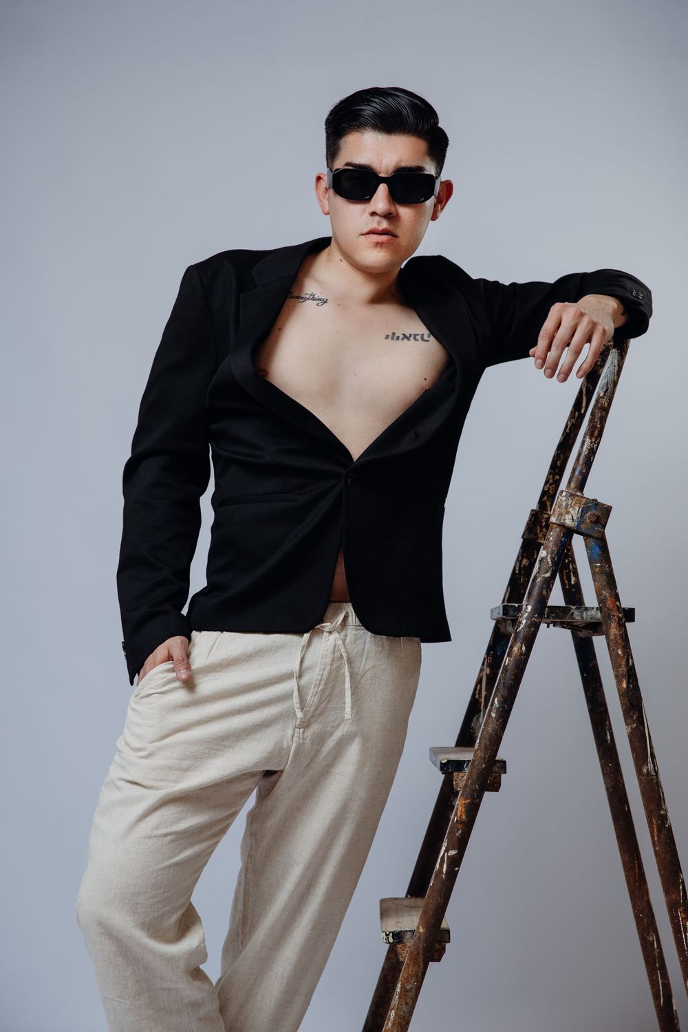 Stylish pose with sunglasses and blazer next to vintage wooden ladder.
