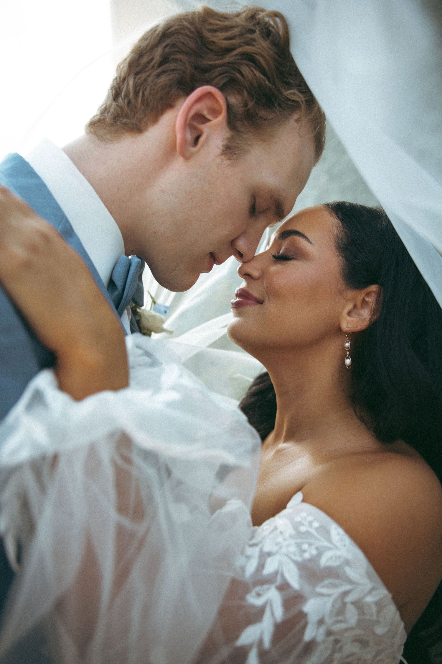 An intimate close-up portrait of newlyweds sharing a tender moment under a veil.