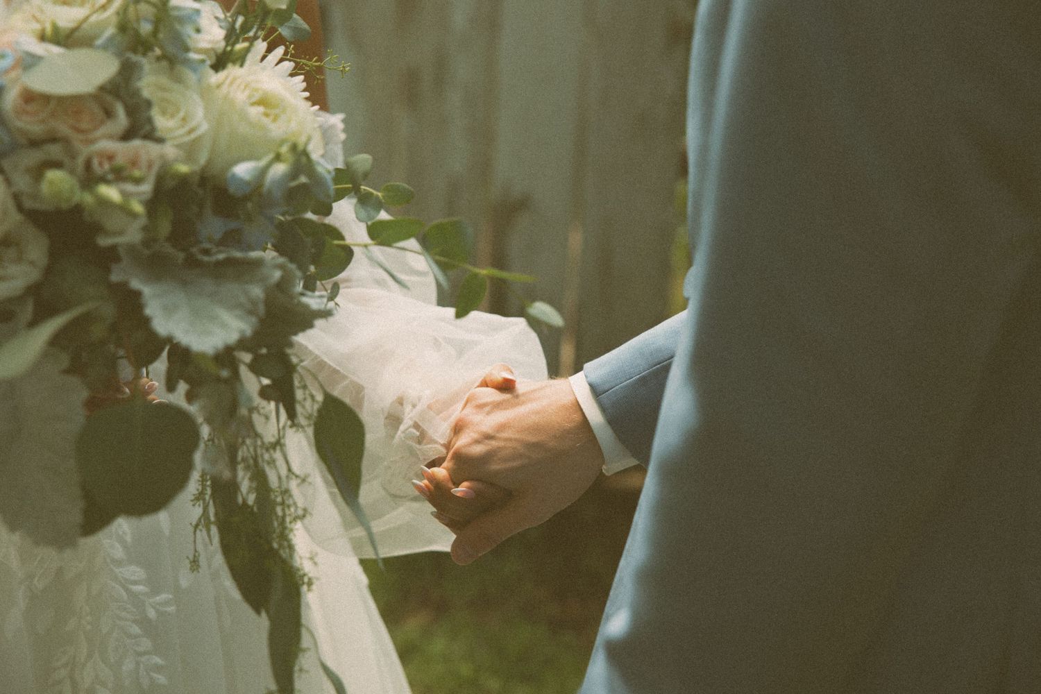 Close-up detail shot of wedding couple's hands holding a white and cream floral bouquet.