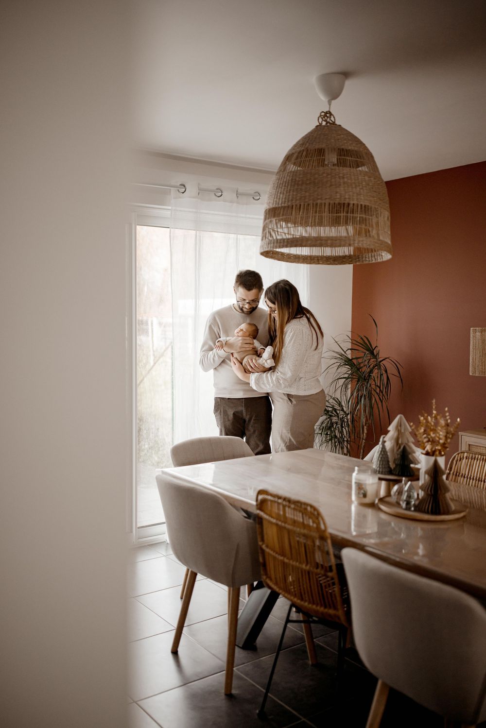 A cozy dining room scene with woven pendant light, modern chairs, and houseplants near sliding glass doors.