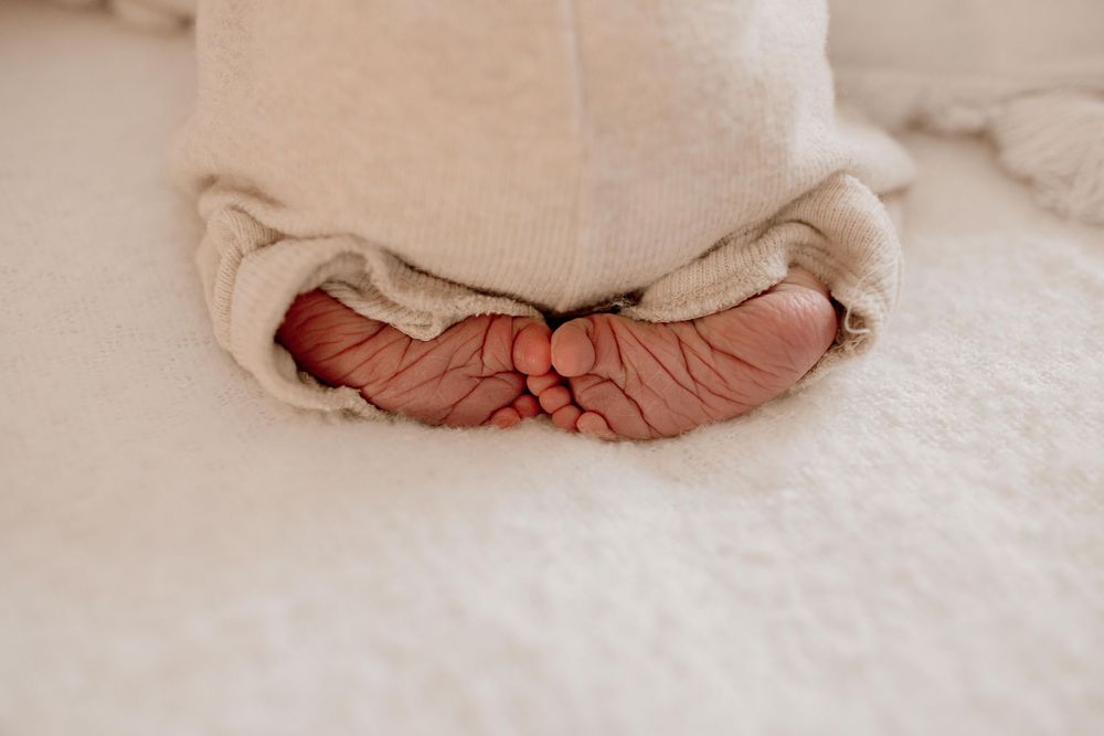 Tiny newborn feet wrapped in soft brown socks peeking out from a cozy white blanket.