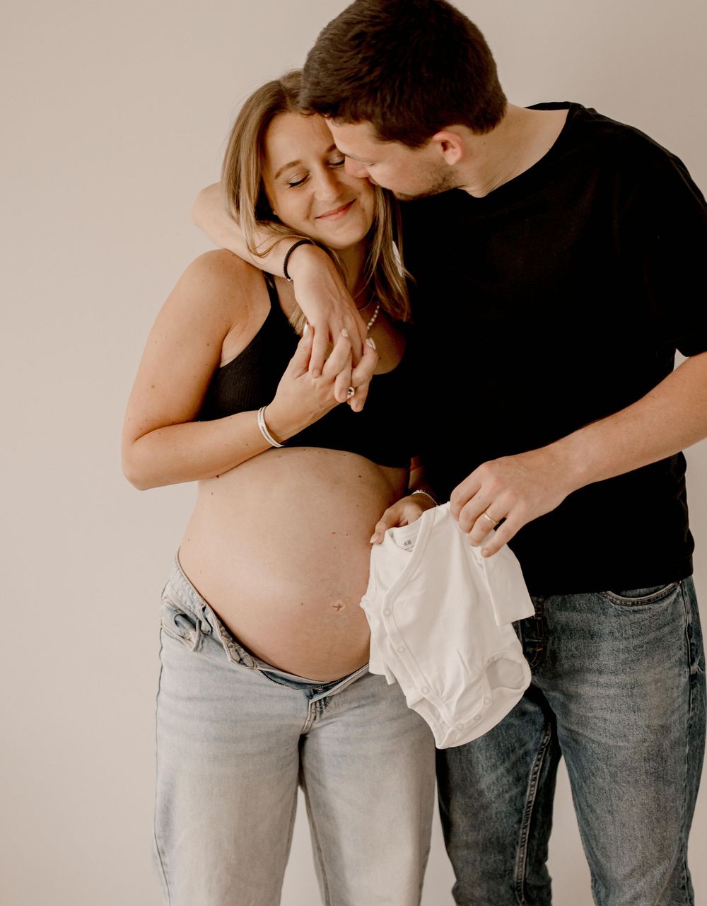 Intimate maternity photo showing a couple in black and denim sharing a tender moment against a neutral background.