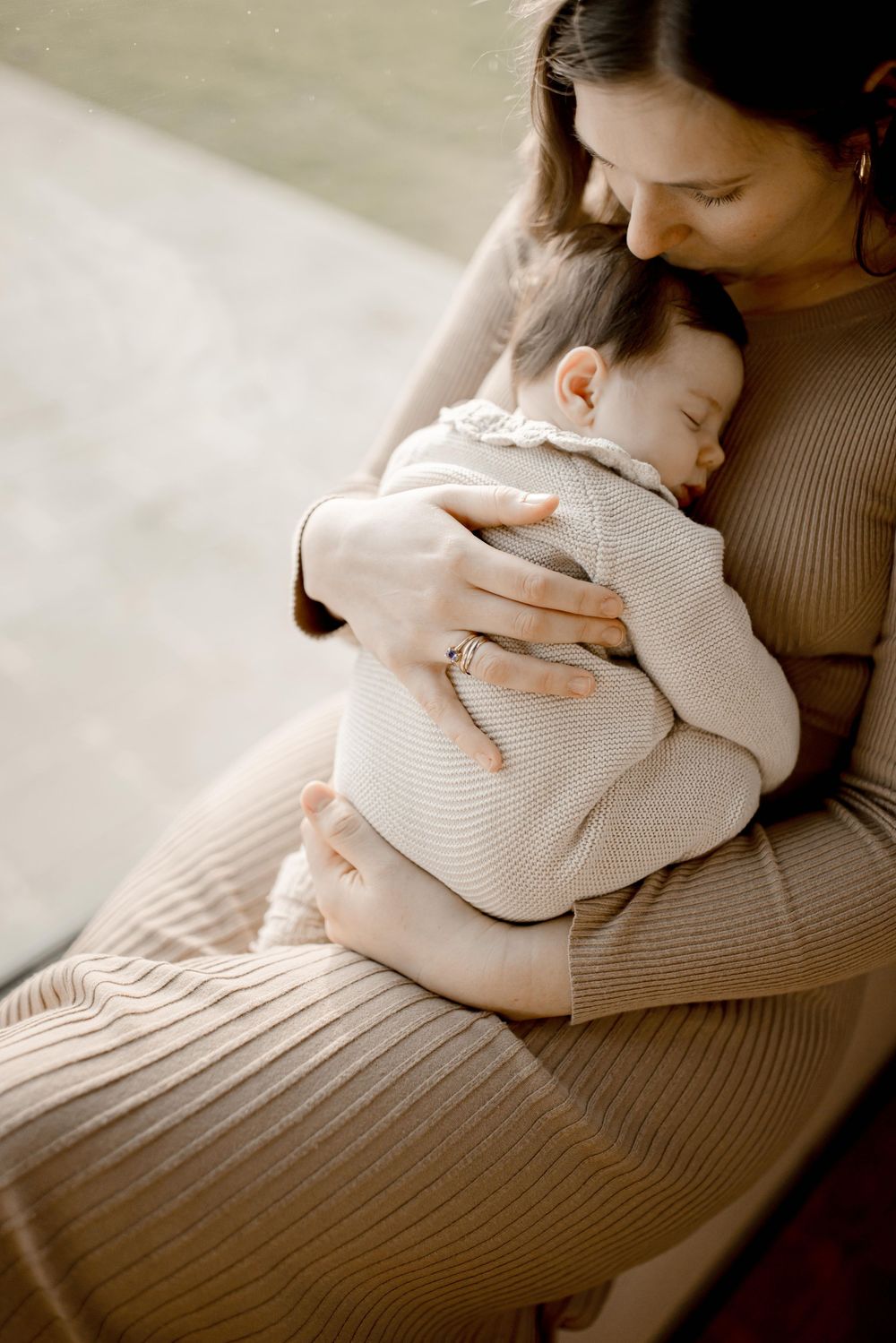 An infant sleeping peacefully in a knit sweater while being cradled in soft natural lighting.