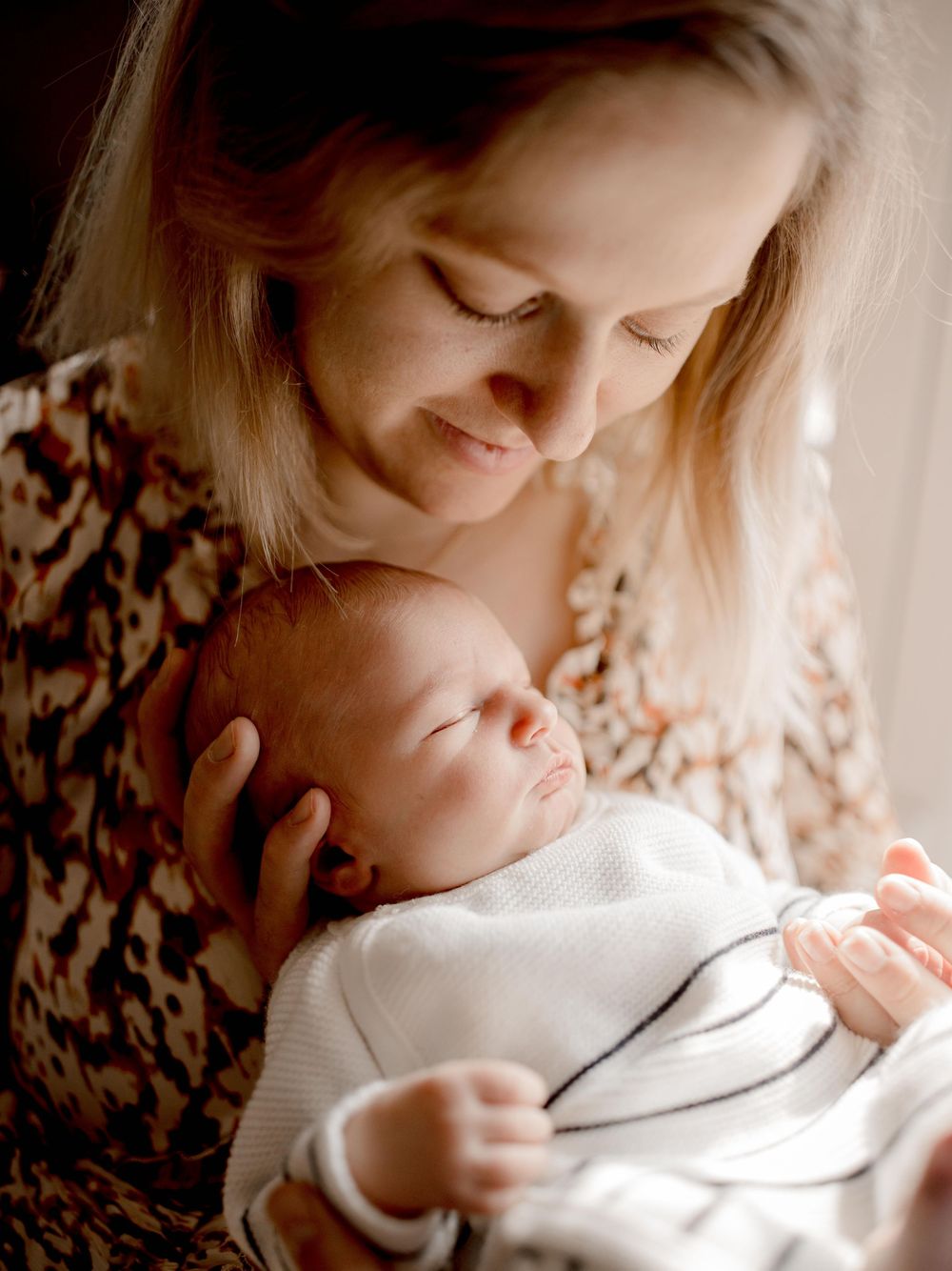 A tender moment captured as a parent in a floral top cradles their peacefully sleeping newborn baby swaddled in white.