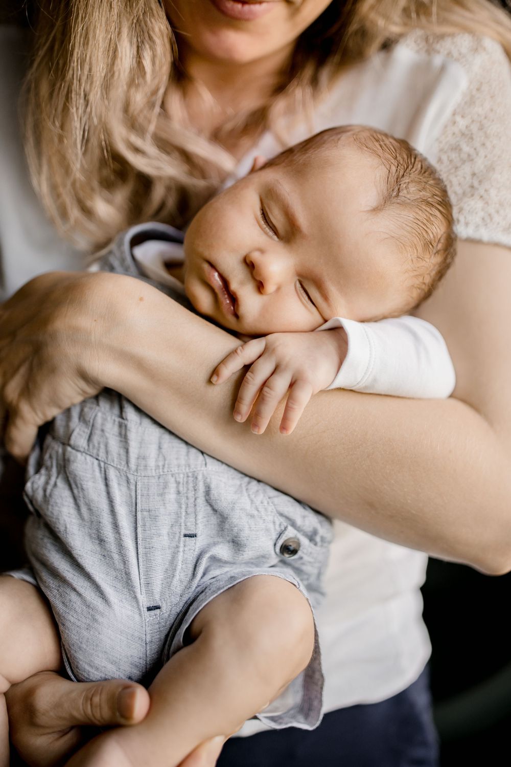 Un bébé endormi en salopette bleue repose paisiblement contre la poitrine de sa maman.