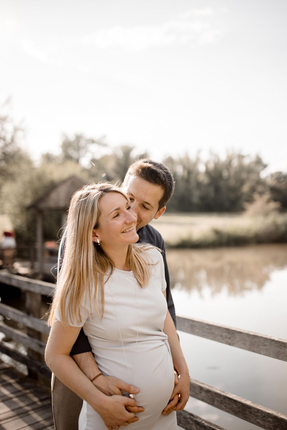 Photo de maternité intime d'un couple enlacé sur un pont en bois au bord d'un lac.