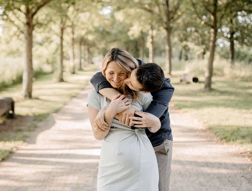 Portrait de maternité romantique en extérieur avec un couple partageant un moment de tendresse sur un chemin bordé d'arbres.