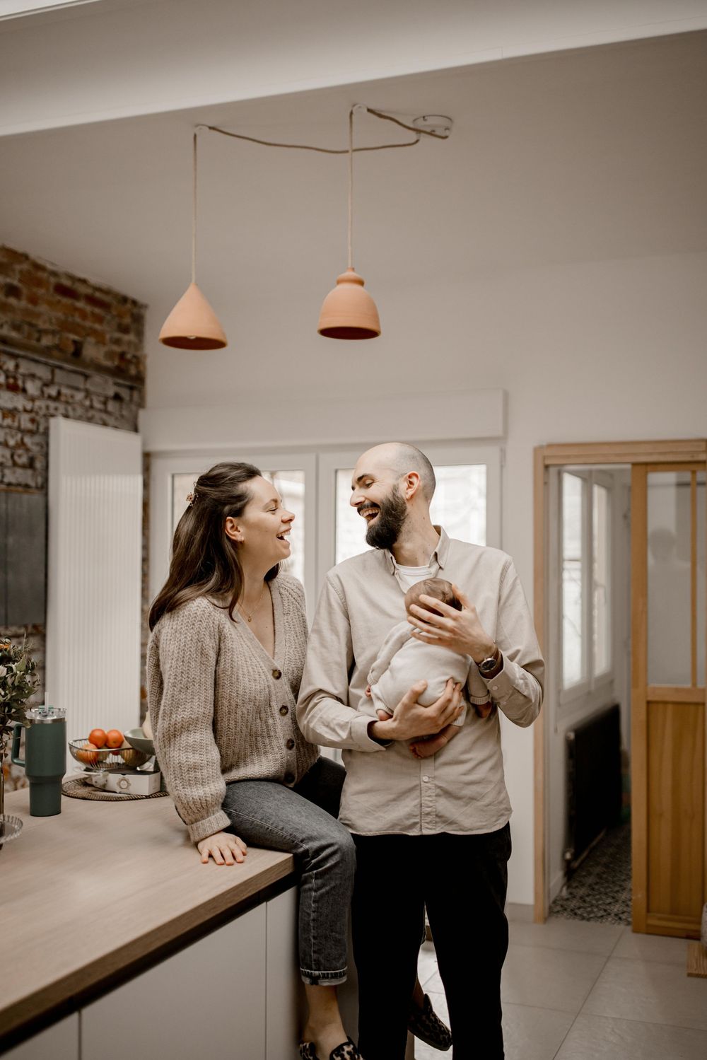 A couple shares a joyful moment together in a modern kitchen with pendant lights and exposed brick walls.