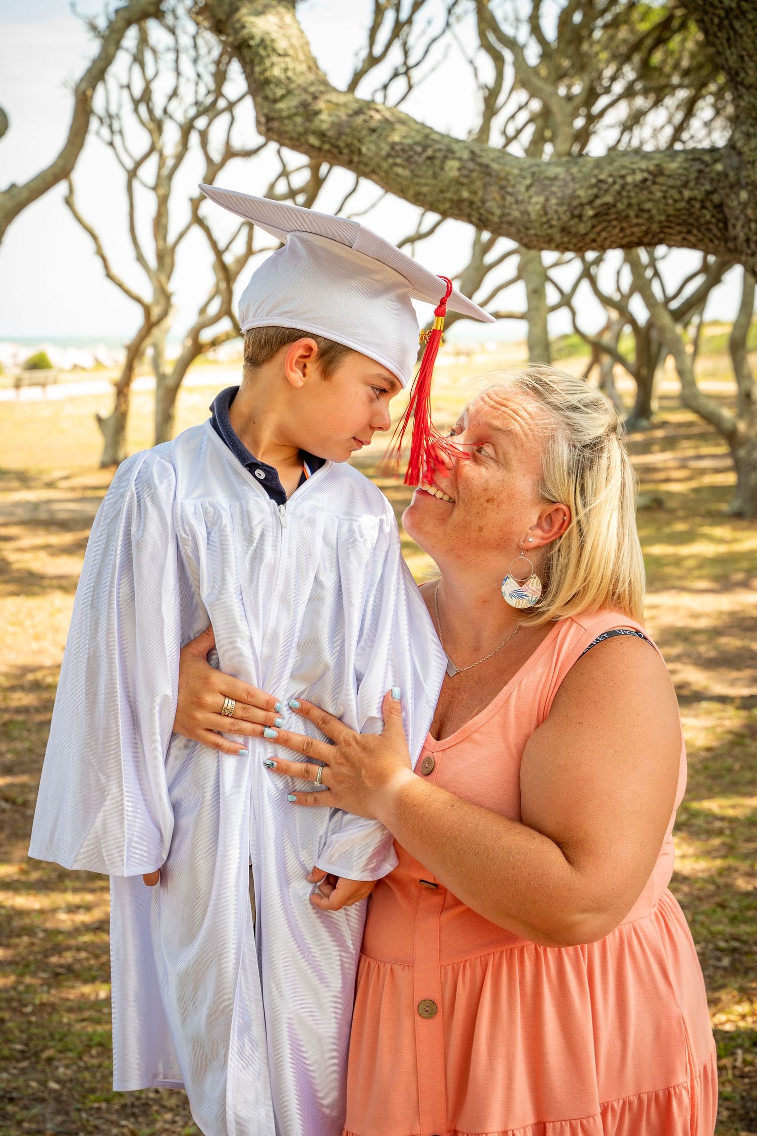 A touching graduation moment captured under a tree with dappled sunlight.