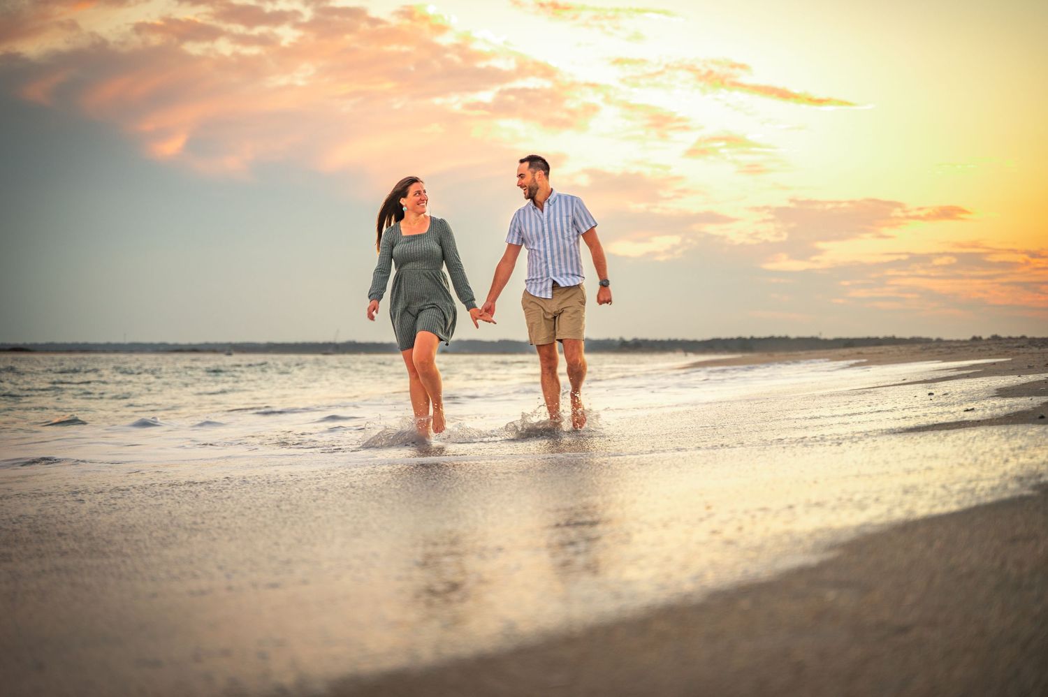 Couple walking hand in hand on beach during golden hour sunset.