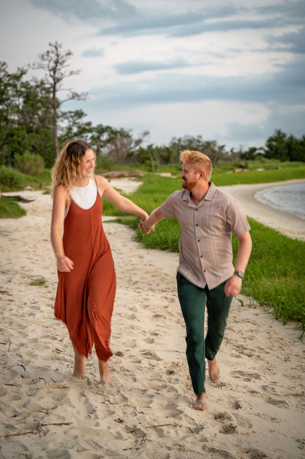 Couple walking barefoot and holding hands along empty beach at sunset.