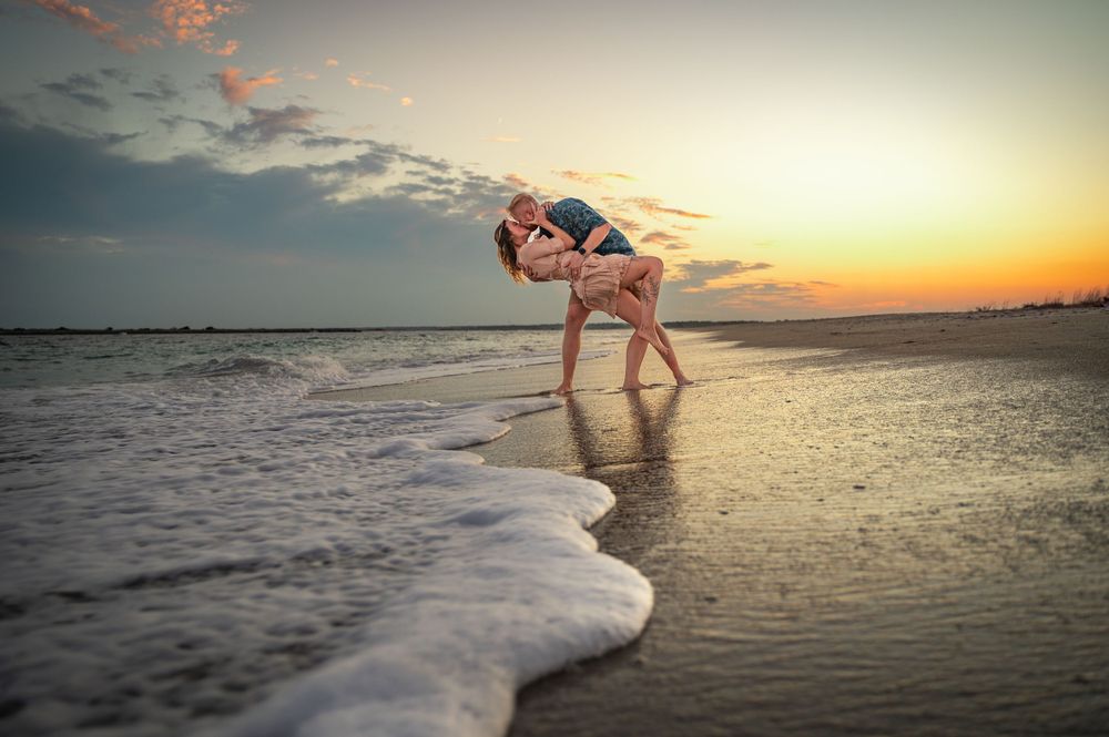 Silhouette of person dancing in shallow ocean water during golden sunset.