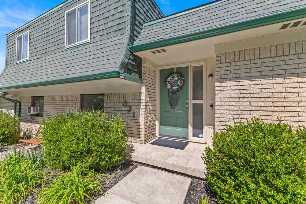 Charming brick townhome exterior with green trim, manicured landscaping, and welcoming front entryway with wreath.