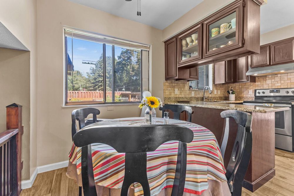 Cozy dining area with dark wood table, kitchen cabinets with glass doors, granite counters, and natural light.
