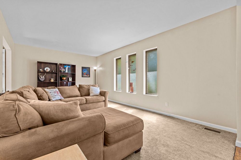 Bright living room with large sectional sofa, neutral walls, and carpeted flooring.