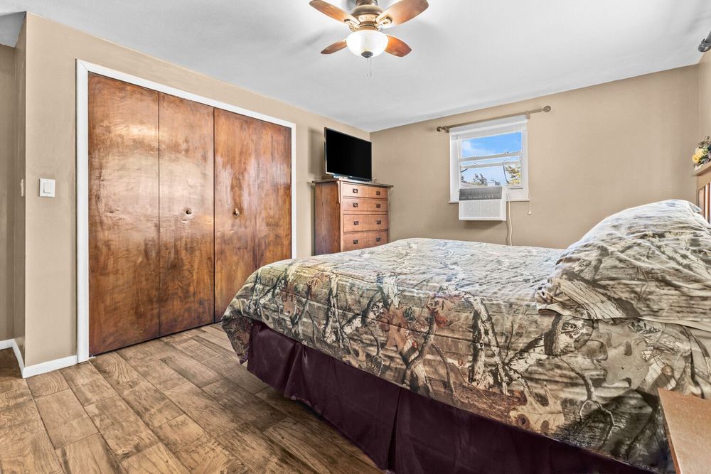Bedroom with hardwood floors, large wooden closet, ceiling fan, dresser, and natural window light.