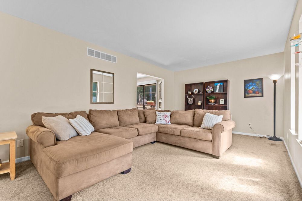 Bright living room with a large sectional sofa, carpeted floors, arched doorway, and neutral wall tones.