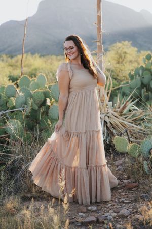 A flowy beige tiered dress photographed against a desert landscape with mountains and cacti in the background.