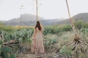 Desert photoshoot featuring a flowing maxi dress among cacti and mountain scenery at golden hour.
