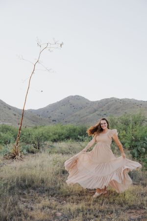 Dramatic dress movement captured against desert mountains and wild vegetation at sunset.