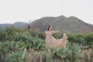 A peachy dress flows in the breeze against a backdrop of mountains and prickly pear cacti.