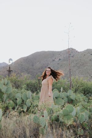 A desert photoshoot features a peach maxi dress among prickly pear cacti and mountain views.