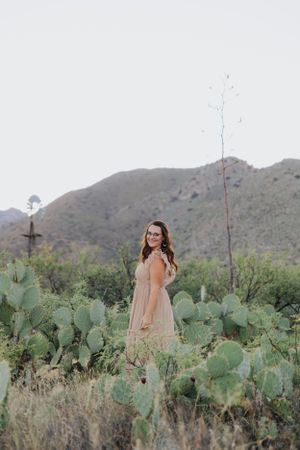 A dreamy desert portrait with mountains and cacti features a flowing peach-colored dress.