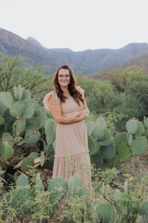 A peaceful desert portrait shows a peach maxi dress surrounded by prickly pear cacti.