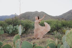 A joyful dance in a flowing peach dress against a desert mountain landscape.