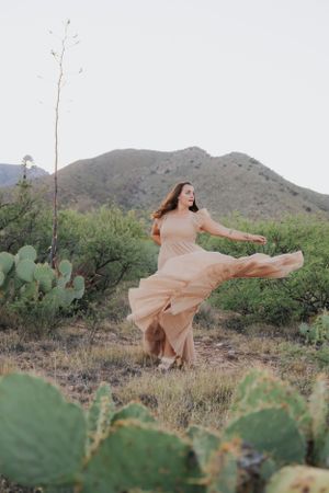 A twirling peach dress creates movement against a backdrop of desert mountains and cacti.