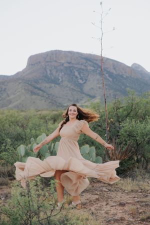A flowing beige dress twirls gracefully against a desert mountain landscape with cacti in the background.