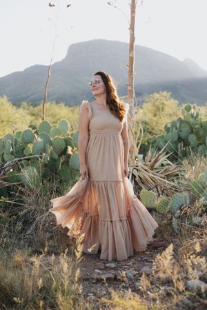 Sunlit desert portrait with flowing dress and mountain scenery.
