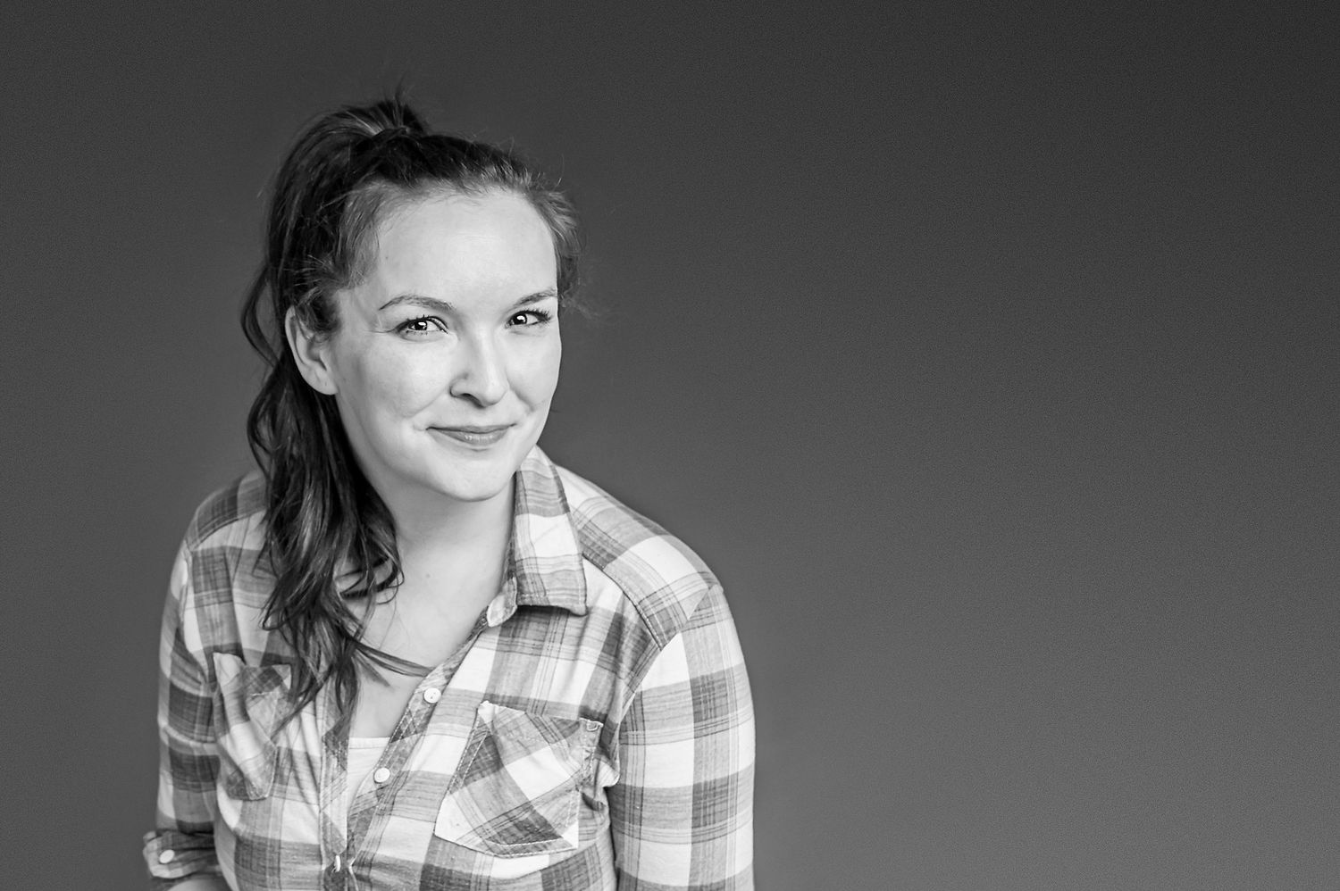 A black and white portrait of someone in a plaid shirt smiling against a dark background.