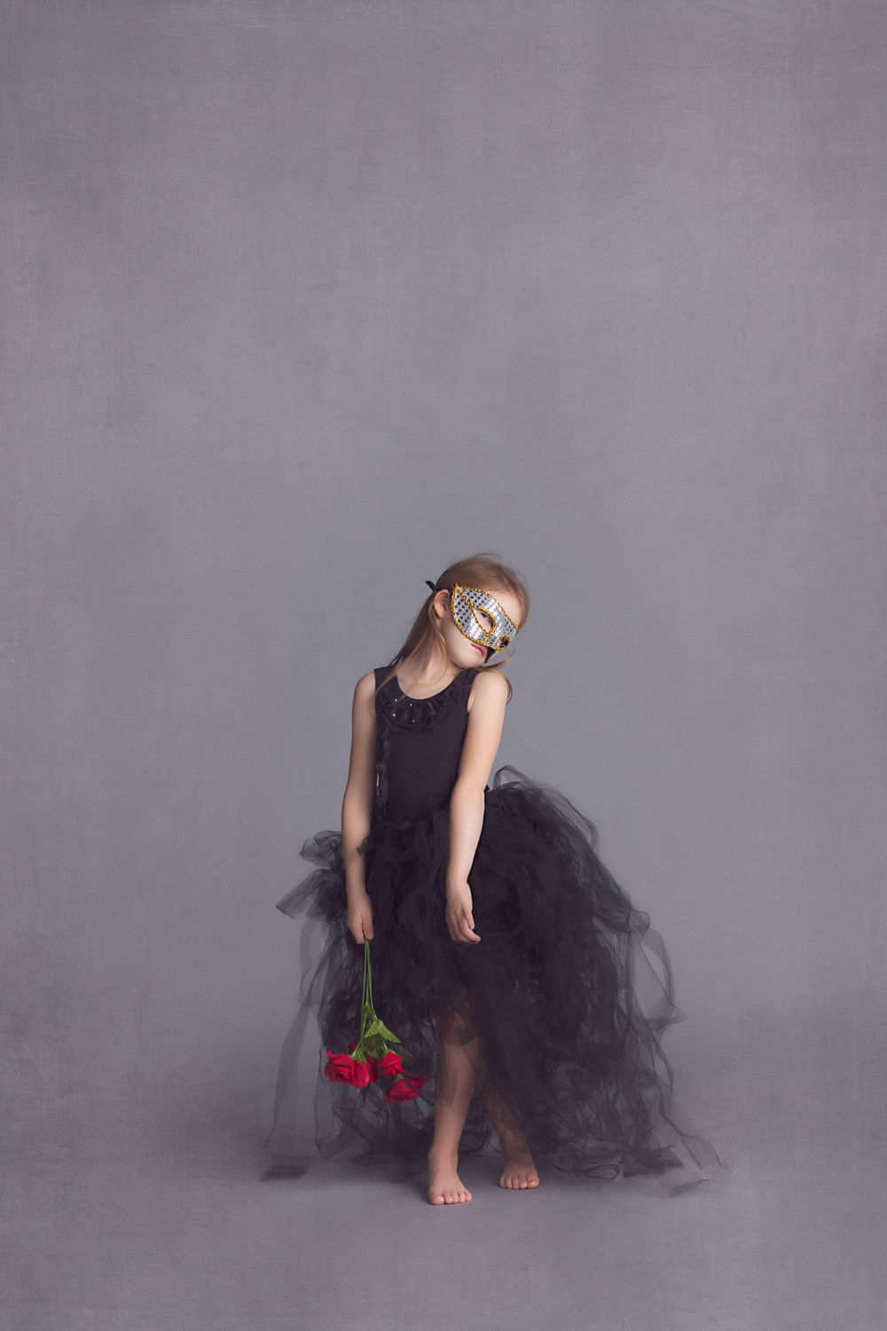 Dancer in black tulle dress holds red roses while posing barefoot.