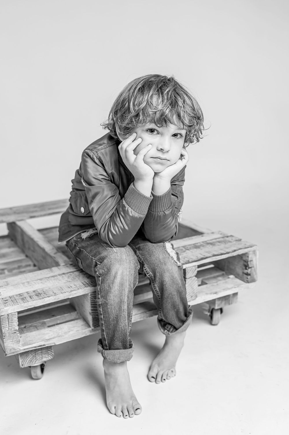 Black and white portrait of contemplative child resting on wooden pallet.