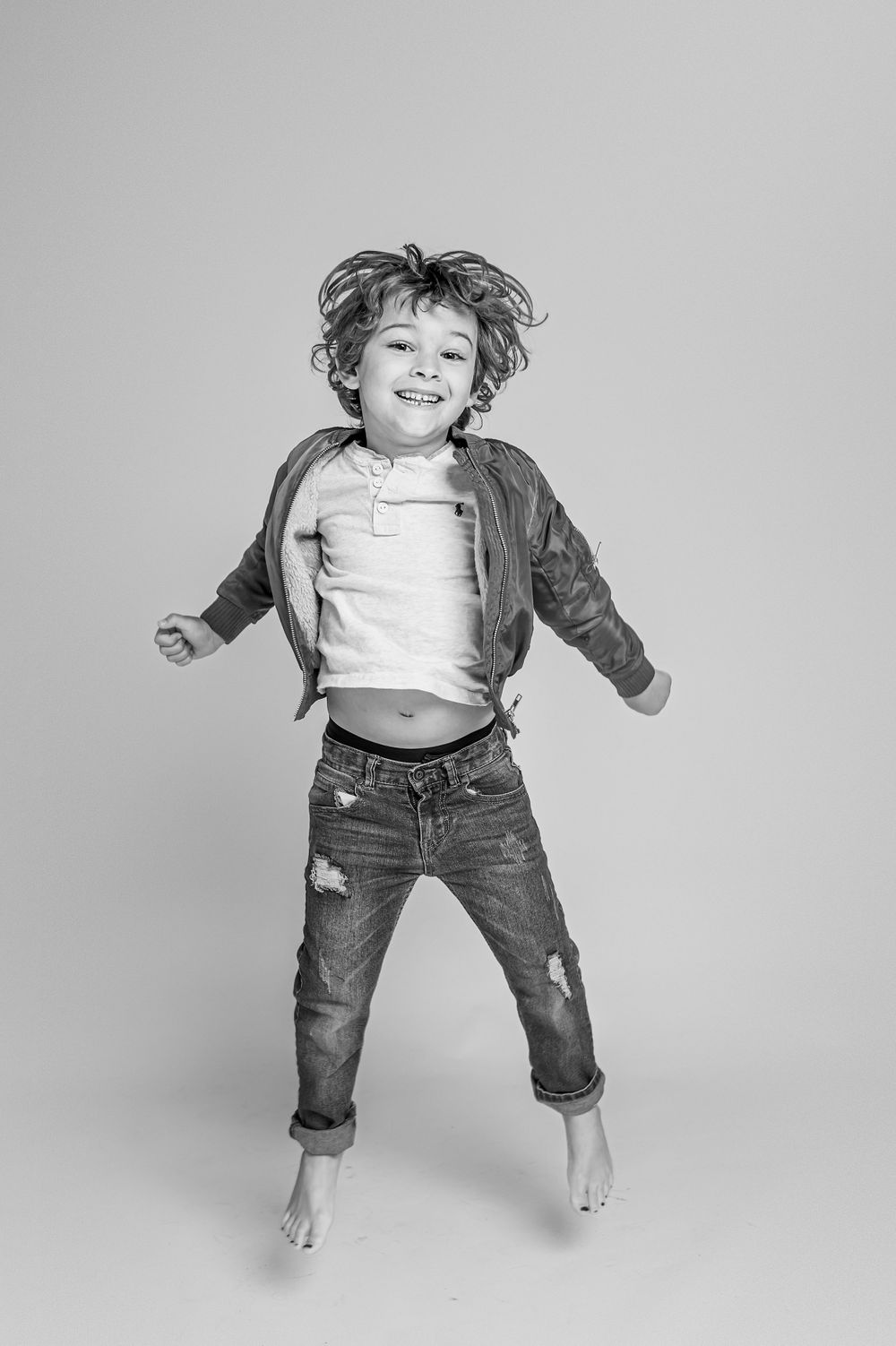 Black and white photo of joyful child jumping in denim and jacket.
