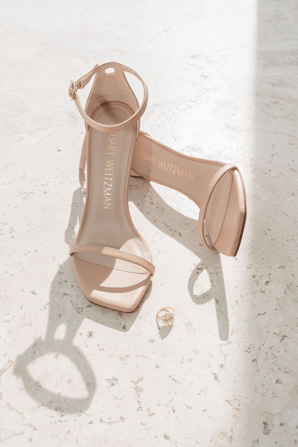 Four stylish nude leather sandals with ankle straps displayed on a white textured surface in different angles.