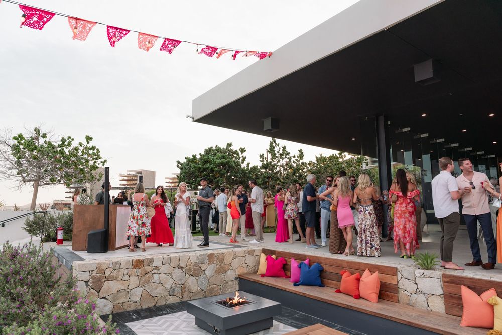 Wedding guests mingling and enjoying drinks at an outdoor reception venue with pink decorative bunting overhead.