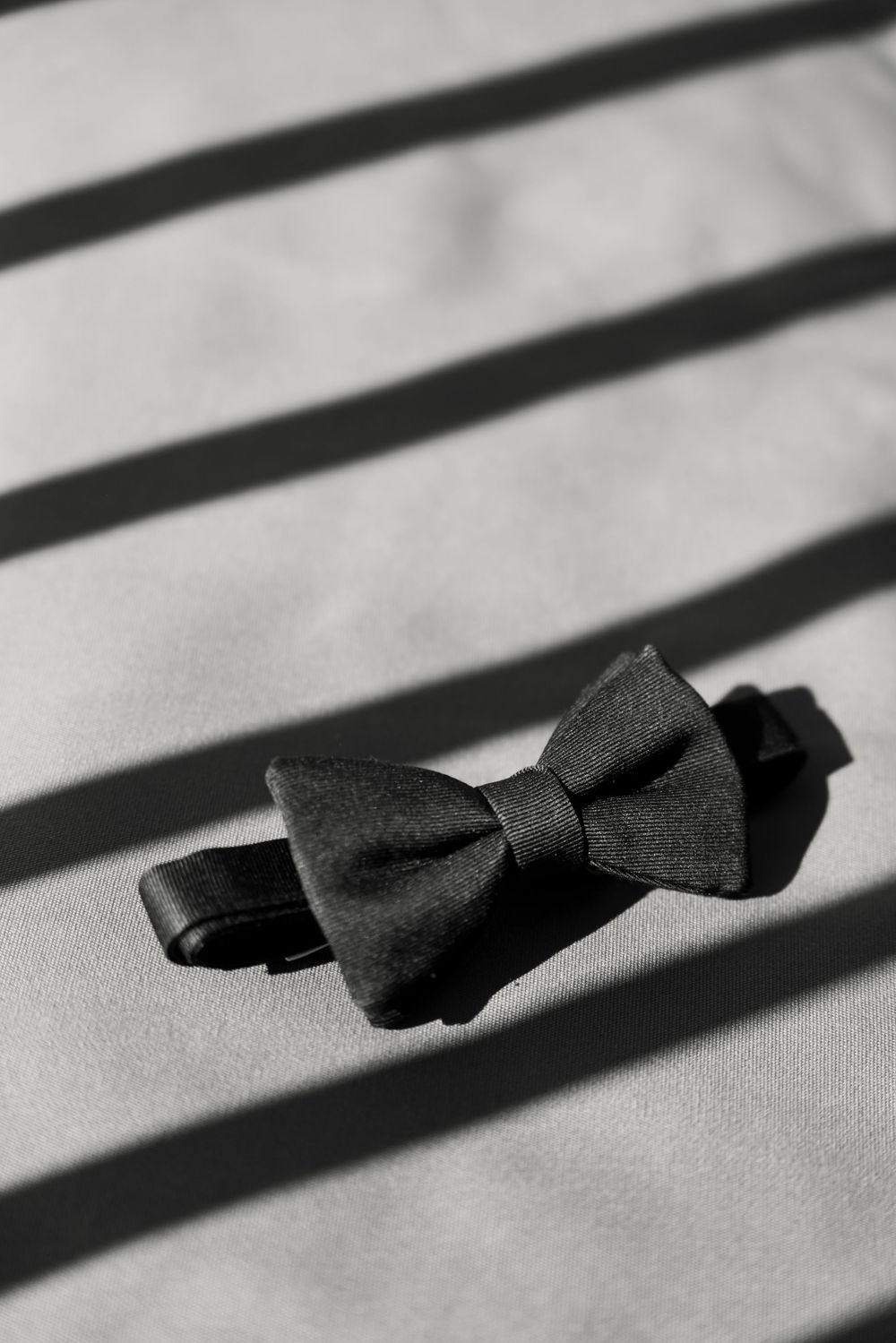 A black bow tie casting diagonal shadows on a white surface creates a striking minimalist composition.