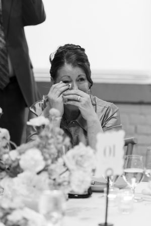 The mother of the bride wipes away a tear with a tissue during speeches at her daughter's reception (B&W).