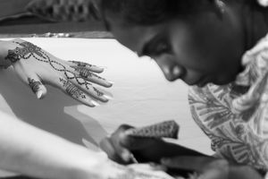 (B&W) A woman artist does henna on another woman's hands.